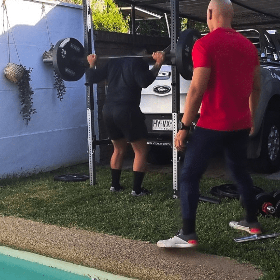 Cliente haciendo sentadillas con ayuda de personal trainer